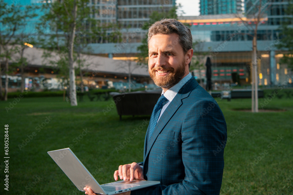 Smiling business man with laptop standing on street near business office building. Businessman front of office. Handsome businessman. Business portrait of serious business man outdoor. Success Smiling business man with laptop standing on street near business office building. Businessman front of office. Handsome businessman. Business portrait of serious business man outdoor. Success