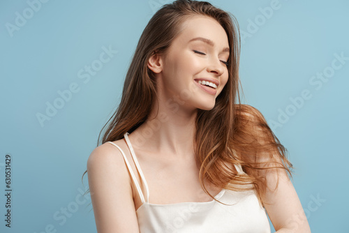 Cute smiling woman with beautiful healthy hair with closed eyes isolated on blue background © Maria Vitkovska
