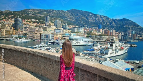 Beautiful girl looking at Port Hercule with Monaco's buildings in background. Young woman enjoys the view of luxury ships, yachts, and deep-water port in the South of France, French Riviera. photo