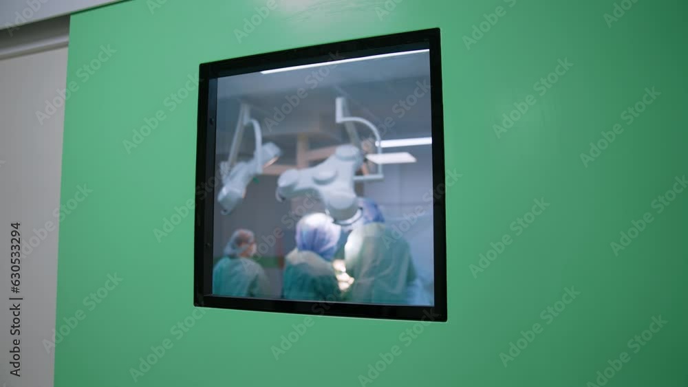 Little window in the door to a surgery room. Doctors' team performing a surgery in the room.
