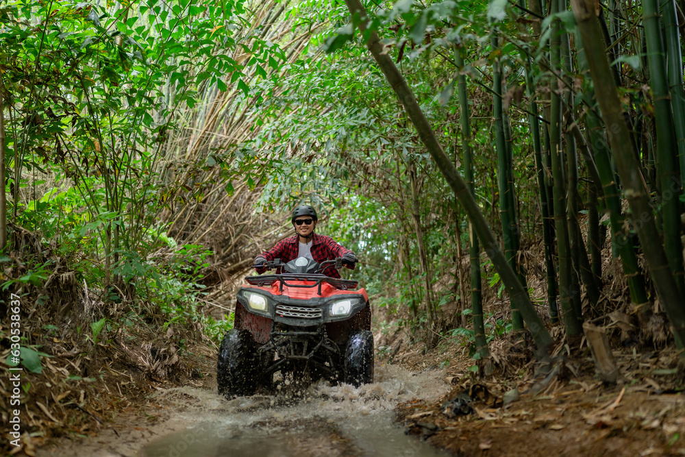 Fototapeta premium Asian guy having fun while driving an atv in the jungle alone. Drive through water in the deep forest.