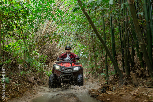 Asian guy having fun while driving an atv in the jungle alone. Drive through water in the deep forest.