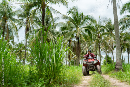 Asian guy having fun while driving an atv in the jungle alone. coconut tree background