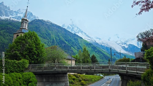 Old French Church and a bridge over the road with Alps mountains in Chamonix. Scenic view of Chamonix-Mont-Blanc during summer with snow on the peak of the mountains in France