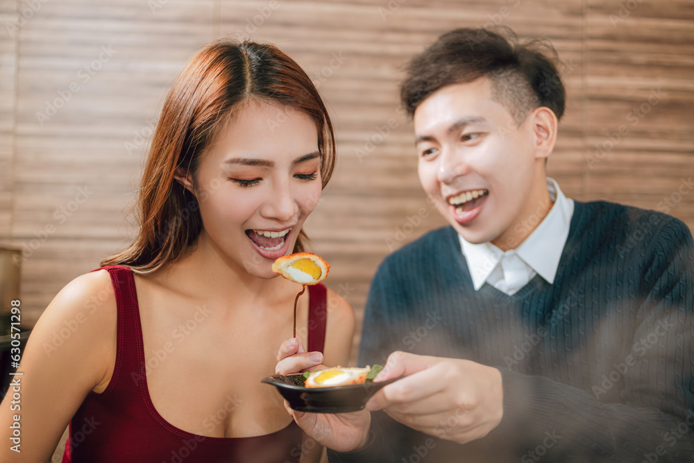 Young asian man feeding happy girlfriend with tasty food in restaurant Young asian man feeding happy girlfriend with tasty food in restaurant