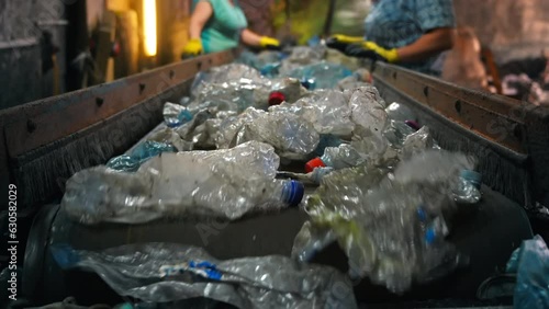 Plastic garbage on a conveyor belt at waste recycling factory. Workers on the background