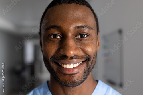 Portrait of happy african american male doctor wearing scrubs in corridor at hospital