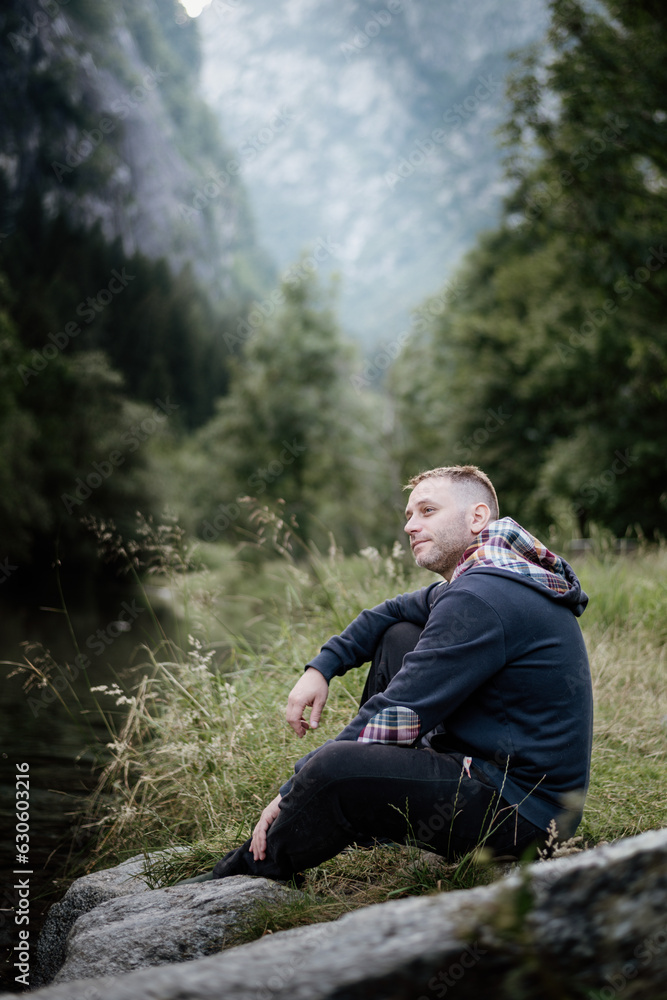 Forty-year-old man sitting on a rock in the mountains in the forest. Adventure during vacation. Outdoor activities and relaxation. Forty-year-old man sitting on a rock in the mountains in the forest. Adventure during vacation. Outdoor activities and relaxation.