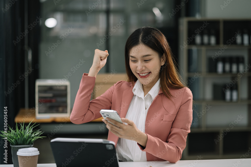 Overjoyed charming excited asian business woman worker using smartphone working in office, feeling happy.