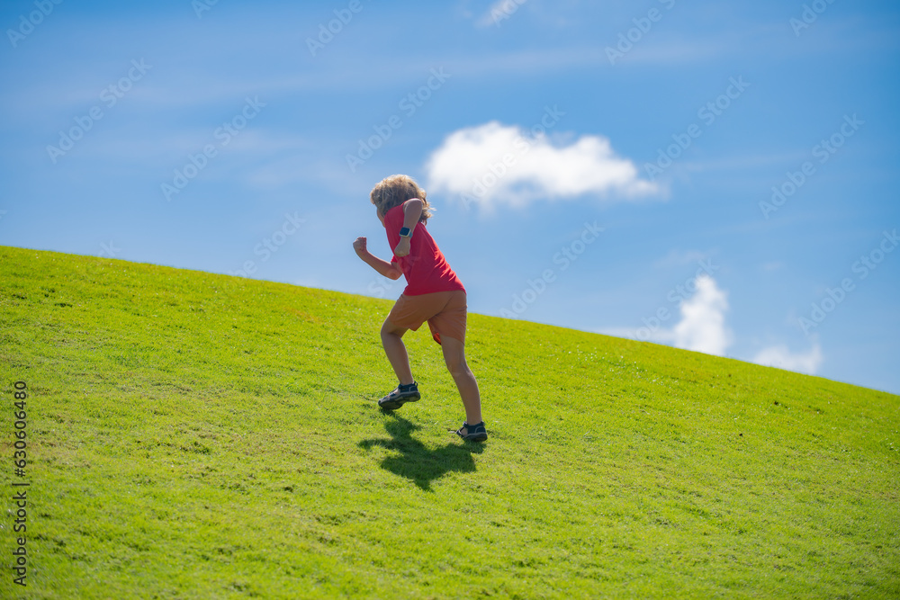 Cute boy running on green grass and blue sky. Kid boy running outdoor. Sport for children. Runner kids race in park.