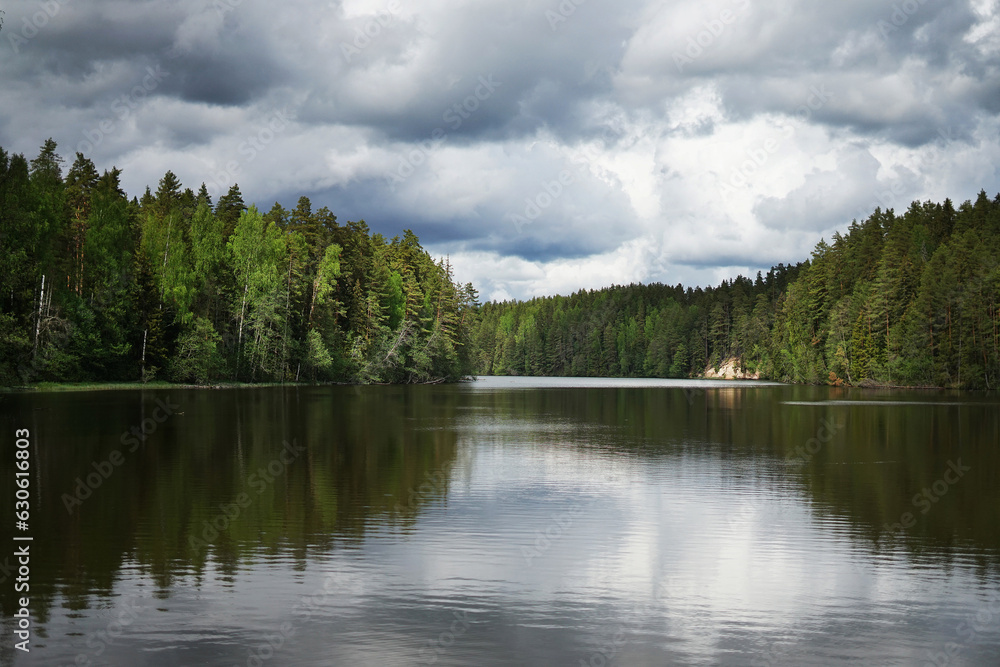Grey rainy clouds over a large forest lake surrounded by evergreen trees