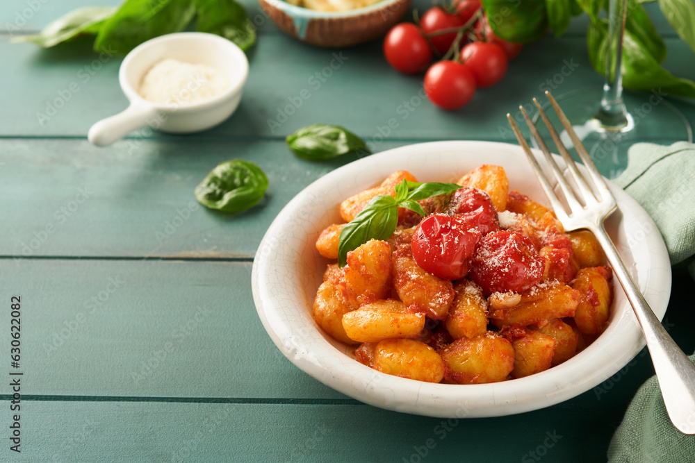 Potato gnocchi. Traditional homemade potato gnocchi with tomato sauce, basil and parmesan cheese on turquoise rustic kitchen table background. Traditional Italian food. Top view.