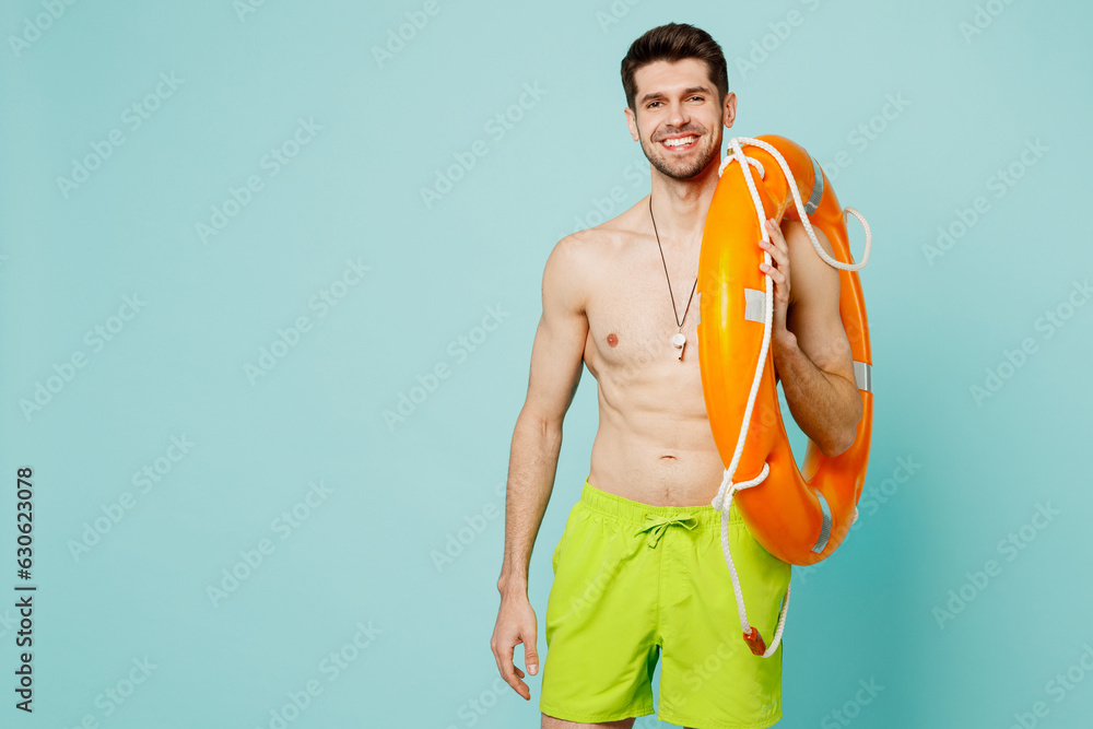 Young happy cool man wear green shorts swimsuit whitsle relax near hotel pool hold in hand lifebuoy look camera isolated on plain light blue cyan background. Summer vacation sea rest sun tan concept.