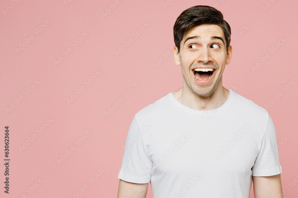 Young surpirsed shocked man wear white t-shirt casual clothes look aside on workspace area mock up with opened mouth isolated on plain pastel light pink background studio portrait. Lifestyle concept. Young surpirsed shocked man wear white t-shirt casual clothes look aside on workspace area mock up with opened mouth isolated on plain pastel light pink background studio portrait. Lifestyle concept.