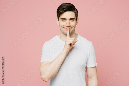 Young secret caucasian man wearing white t-shirt casual clothes say hush be quiet with finger on lips shhh gesture isolated on plain pastel light color background studio portrait. Lifestyle concept.