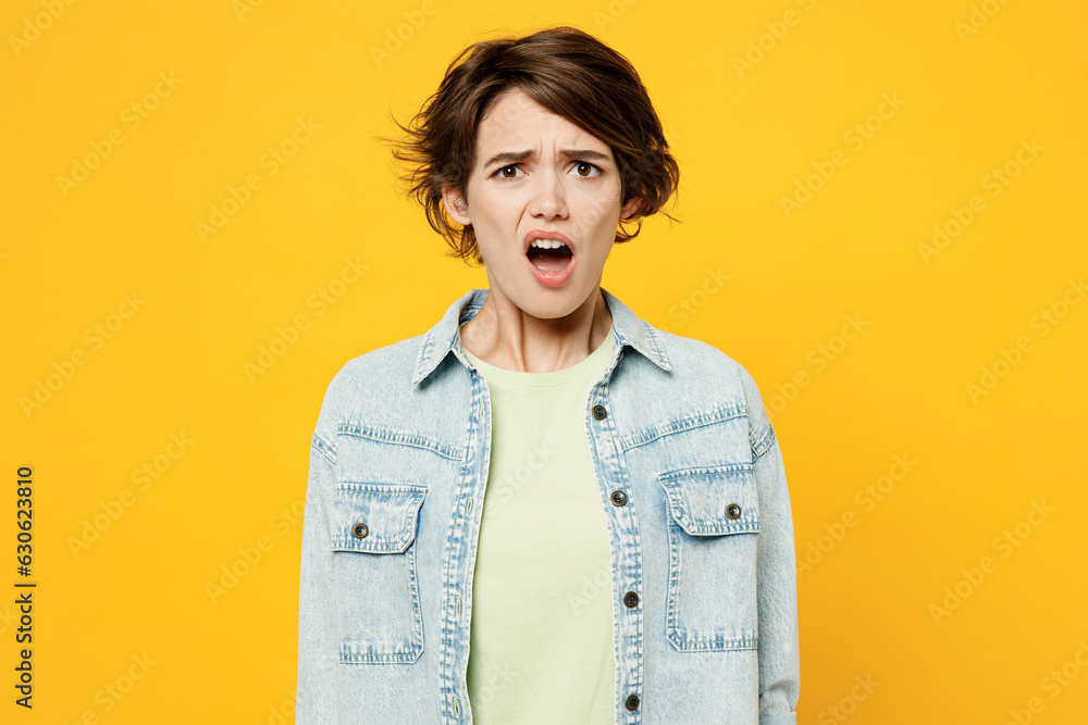 Young sad dissatisfied unhappy displeased woman she wear green t-shirt denim shirt casual clothes look camera with opened mouth isolated on plain yellow background studio portrait. Lifestyle concept. Young sad dissatisfied unhappy displeased woman she wear green t-shirt denim shirt casual clothes look camera with opened mouth isolated on plain yellow background studio portrait. Lifestyle concept.