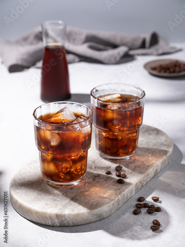 Cold brew coffee in a two glasses with ice on a marble board on a light background with coffee beans, bottle and napkin. Concept summer craft refreshing homemade drink