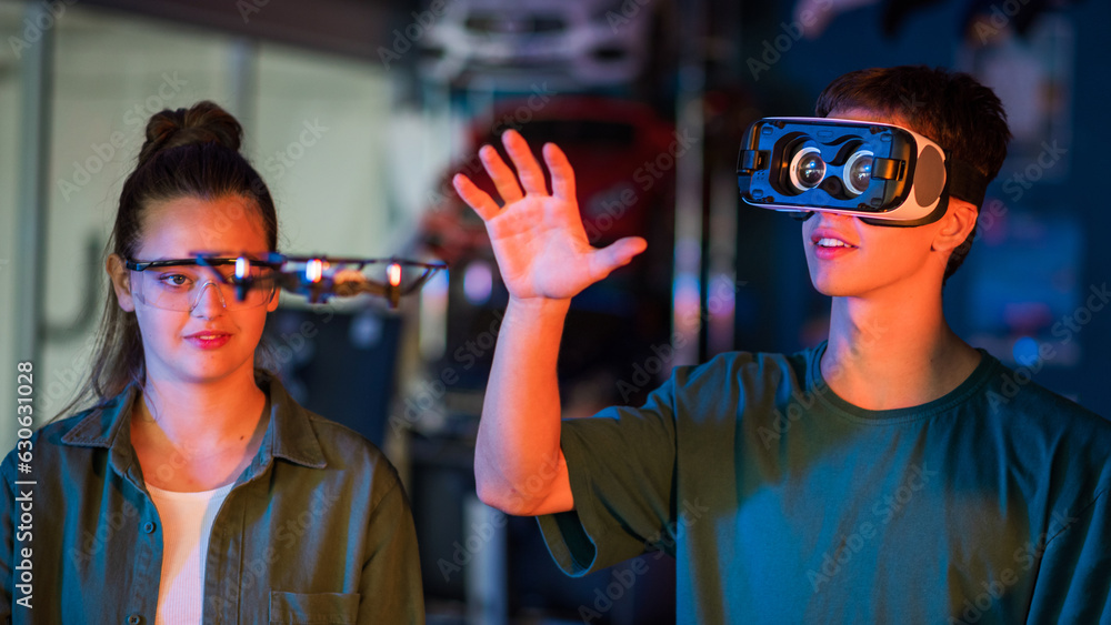 Teens doing experiments in robotics in a laboratory. Boy in VR headset holding a small drone. Red and blue illumination