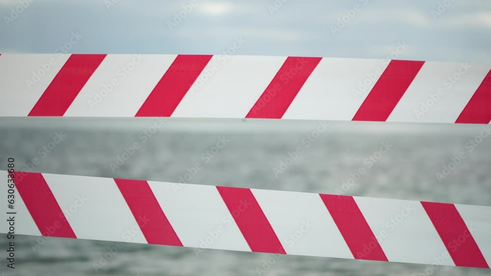 Red white warning tape barrier ribbon swinging in the wind across exotic sea beach background without people. No entry Red White caution tape. No holiday concept, delayed travel, no summer plans Red white warning tape barrier ribbon swinging in the wind across exotic sea beach background without people. No entry Red White caution tape. No holiday concept, delayed travel, no summer plans