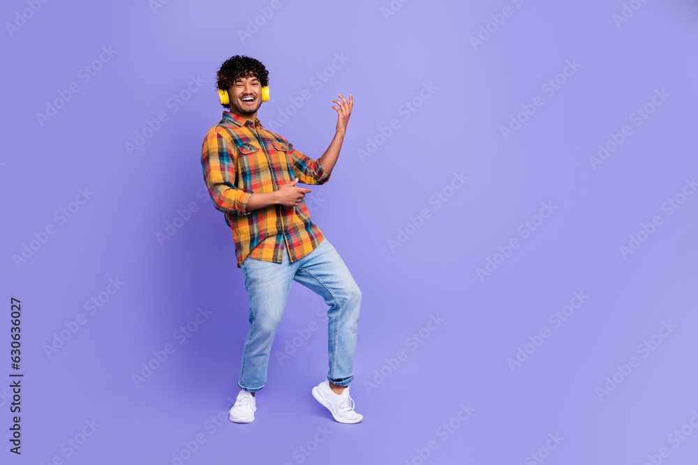Full body photo of young guy playing hands guitar listen rock roll music wireless modern headphones isolated on purple color background Full body photo of young guy playing hands guitar listen rock roll music wireless modern headphones isolated on purple color background