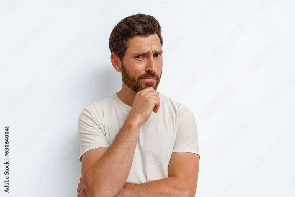 Handsome man holds his hand at his chin and looks thoughtfully at camera on white background Handsome man holds his hand at his chin and looks thoughtfully at camera on white background