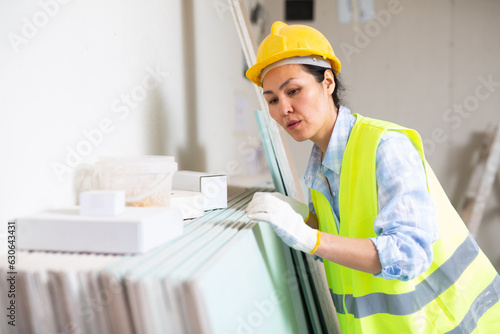 Portrait of a focused woman builder in a hardhat and vest, attentivelly checking the construction panels © JackF