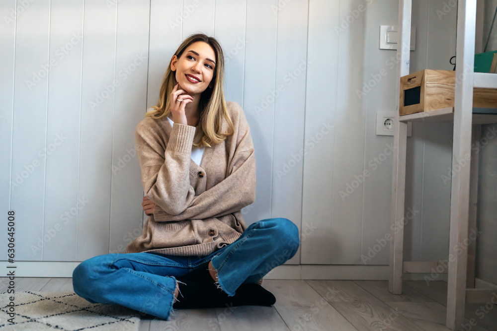 Cheerful young woman smiling while sitting on the floor and planning the design of new apartment Cheerful young woman smiling while sitting on the floor and planning the design of new apartment