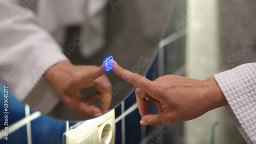 Quadro em tela Woman hand turns on backlight of mirror in bathroom by pressing touch button on and off