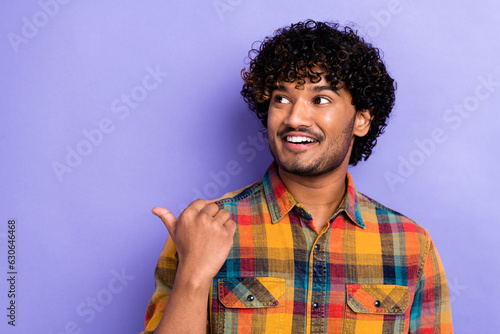 Photo of cheerful nice young man beaming smile look indicate thumb finger empty space isolated on violet color background