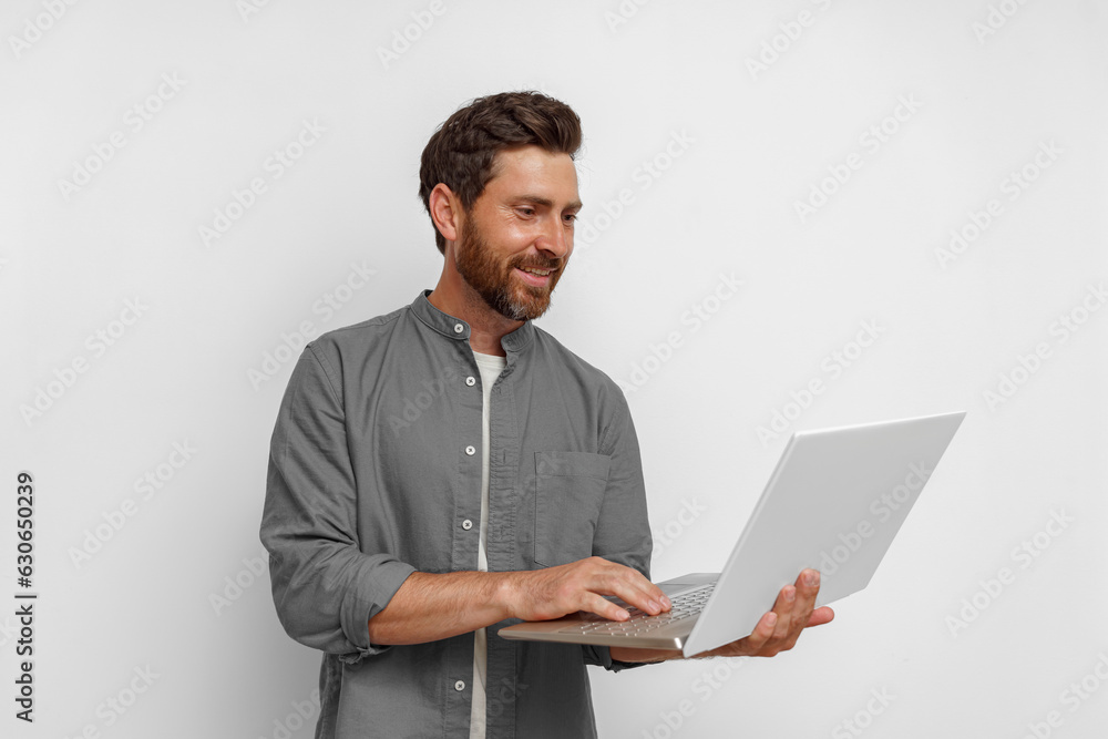 Smiling male entrepreneur working on laptop while standing on white background Smiling male entrepreneur working on laptop while standing on white background