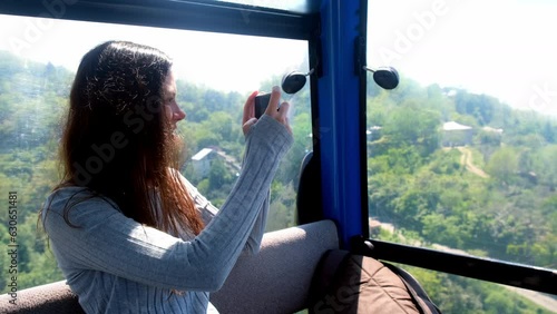 Woman tourist recording video on smartphone sitting in funicular of cable car in mountains. Pretty happy brunette female exploring world travelling in Georgia, Batumi. Travel, tourist, wanderlust. photo