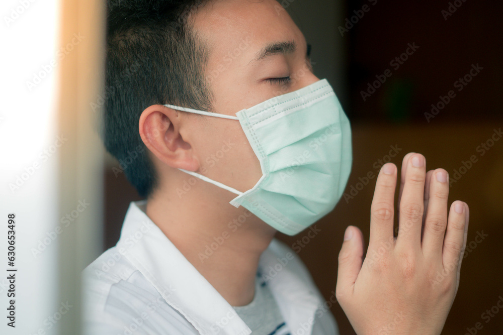 Asian man wearing mask to protect coronavus COVID-19 and pm2.5. Praying and worship to god. Asian may praying at home. Stay at home concept. Social distancing and isolated. Asian man wearing mask to protect coronavus COVID-19 and pm2.5. Praying and worship to god. Asian may praying at home. Stay at home concept. Social distancing and isolated.