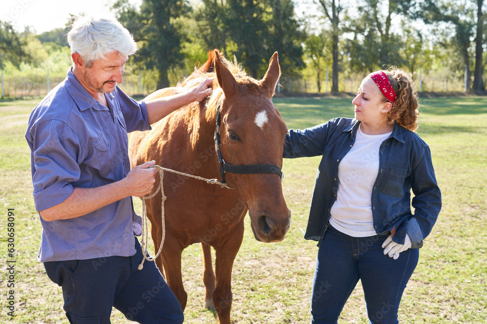 Woman and man holding brown horse on ranch Woman and man holding brown horse on ranch