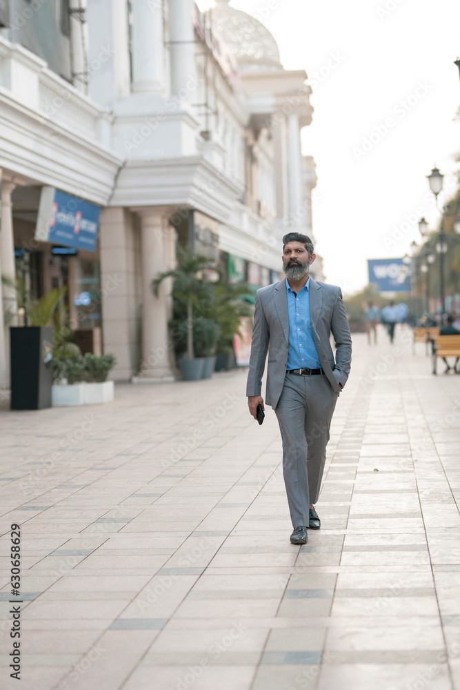 Confident Indian businessman in suit outfit walking on street.