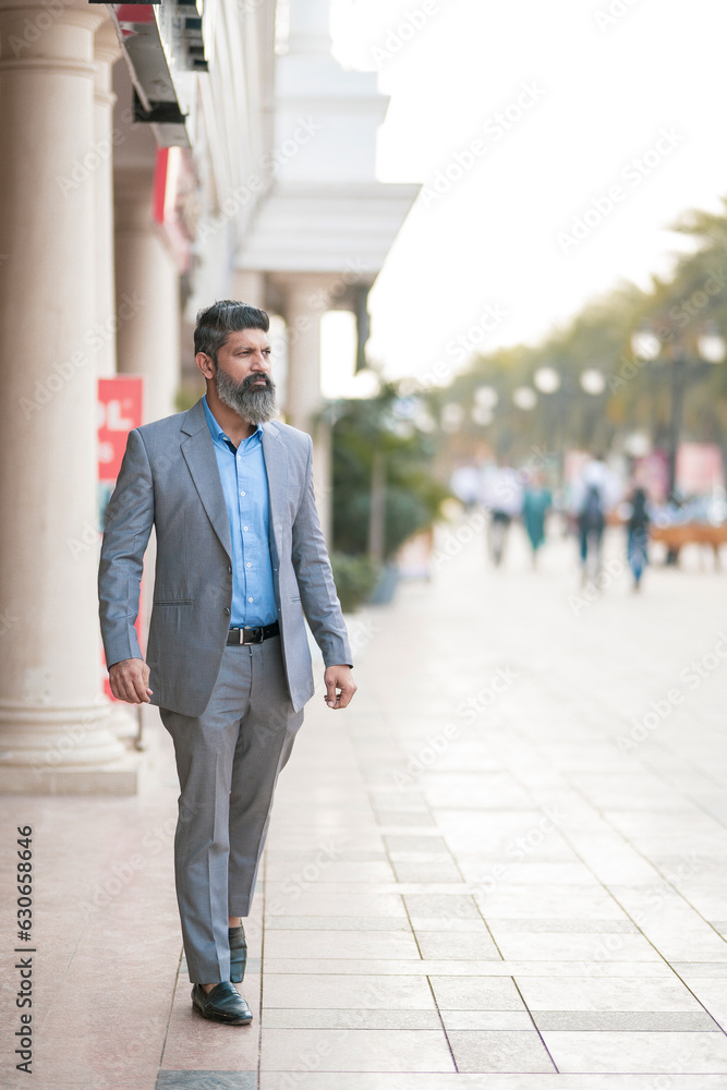 Confident Indian businessman in suit outfit walking on street. Confident Indian businessman in suit outfit walking on street.