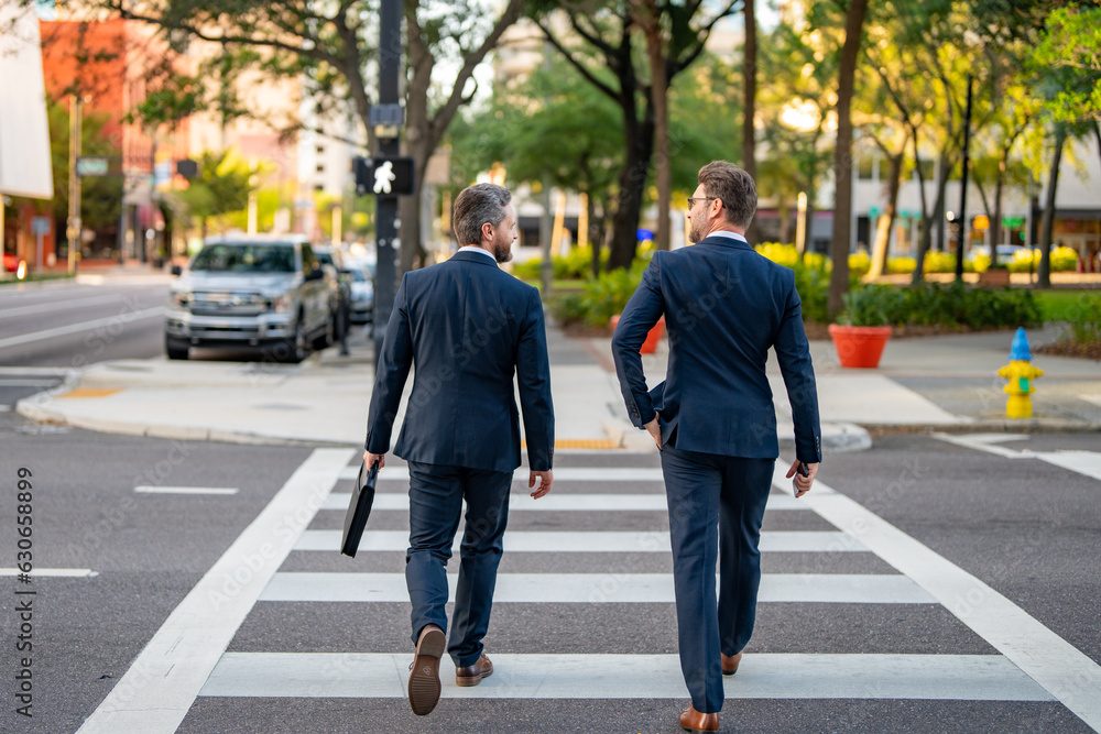 Two elegant businessmen walking outdoors together in the streets with office building. Business men walking outdoors together in the street discussing and chatting. Businessmen from work.