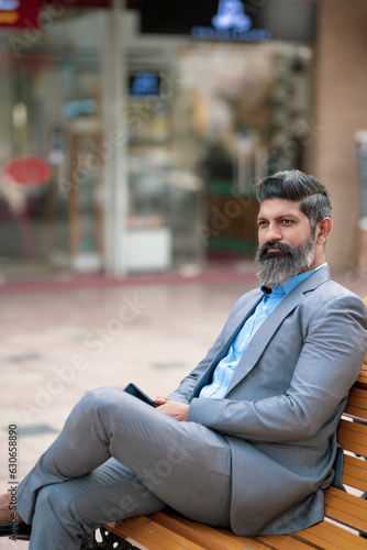 Confident Indian corporate man sitting on bench at street side