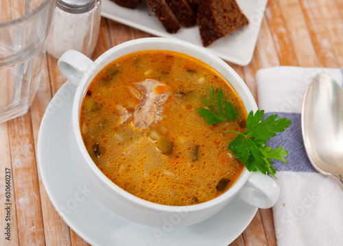 Traditional Russian dish is Pickle soup with meat, cooked on the basis of pickled cucumbers and pearl barley or rice, decorated ..with a sprig of parsley on top