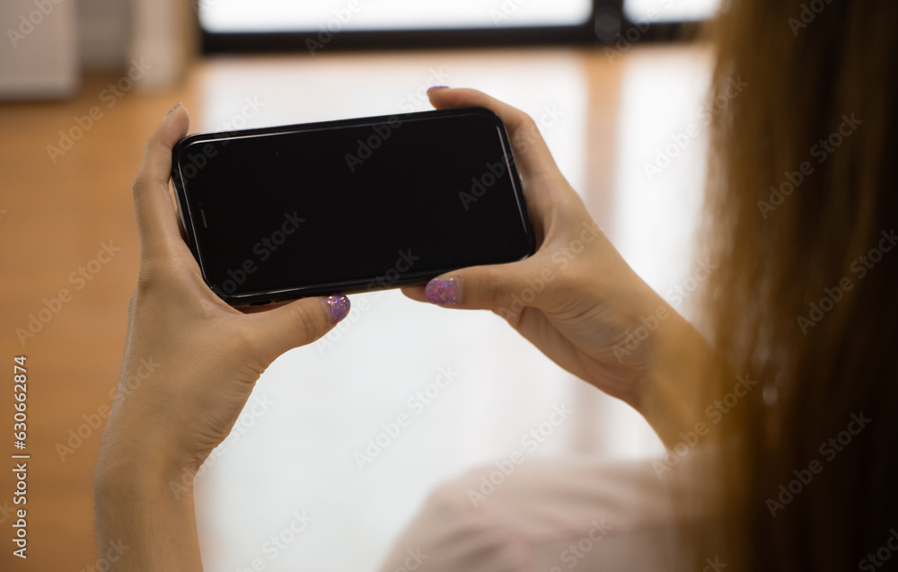 Woman holding mobile phone with blank black screen. Mockup template for artwork design.