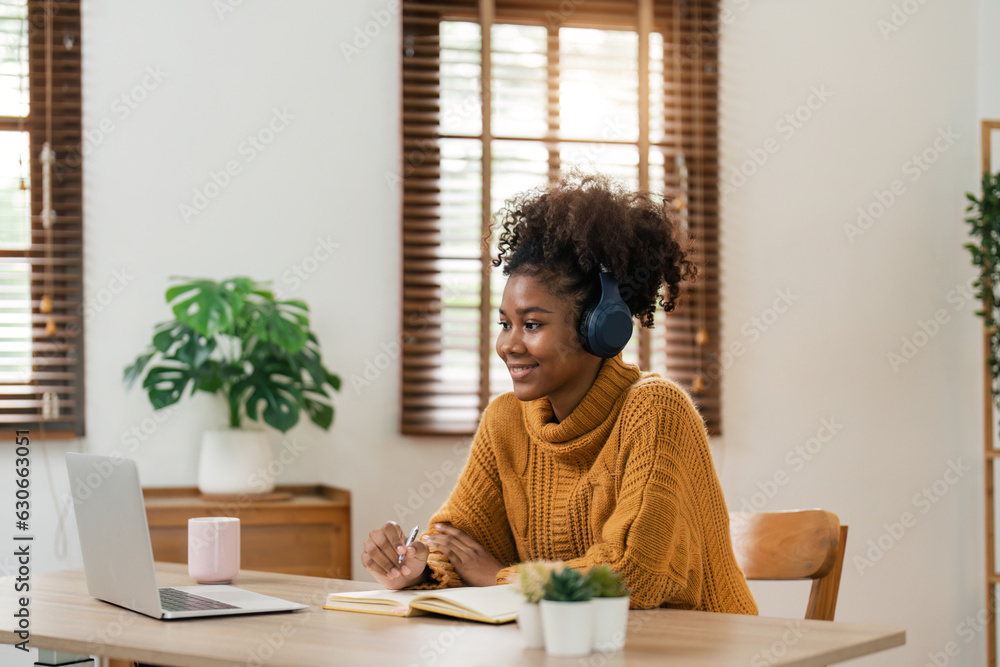Distance Education. Portrait of smiling woman african american sitting at desk, using laptop and writing in notebook, taking notes, watching tutorial, lecture or webinar, studying online at home Distance Education. Portrait of smiling woman african american sitting at desk, using laptop and writing in notebook, taking notes, watching tutorial, lecture or webinar, studying online at home
