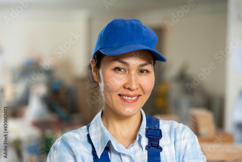 Portrait of positive builder woman in blue overalls next to a stepladder