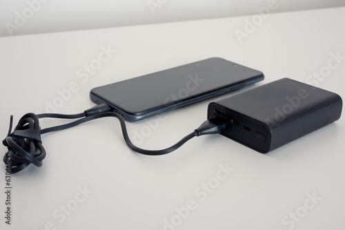 Black power bank charges mobile phone. Black cable