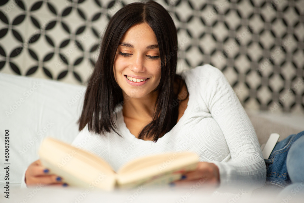 smiling young woman relaxing in bed reading book smiling young woman relaxing in bed reading book