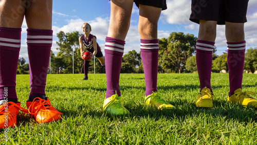 three pairs of legs in football boots and long socks standing on grassed oval