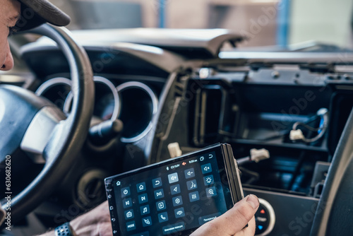 Auto electrician or repairman in car service installs multimedia sound system or car radio in auto dashboard panel. © DedMityay