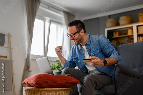 Obraz na plátně Businessman with credit card pumping fist and screaming in joy while doing onlin