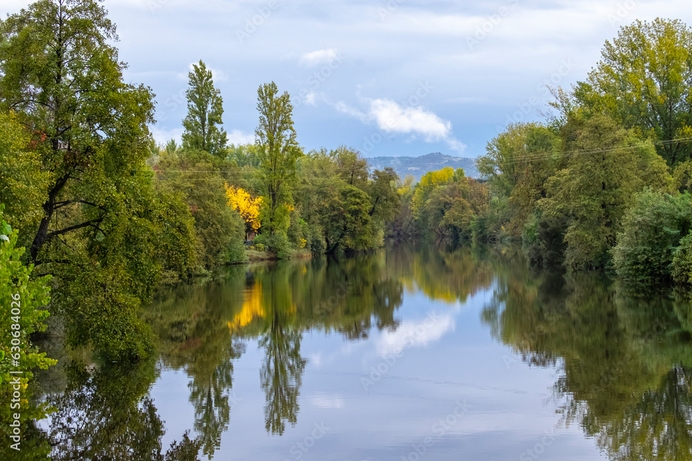 Beautiful landscape of trees on the banks of the Jerte river as it passes through Plasencia, with the mountains of Valle del Jerte in the background.Beautiful nature scenery in Extremadura, Spain