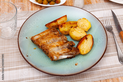 Spicy roasted pork ribs served on plate with vegetable side dish of fried potatoes..