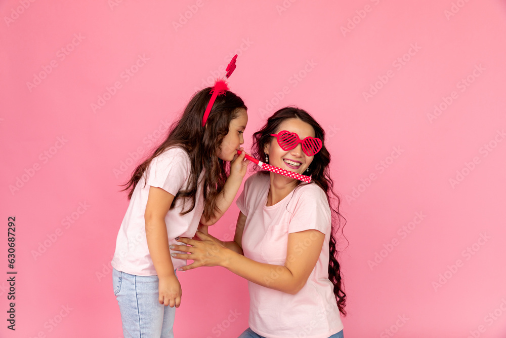 Party concept. Woman in carnival glasses and cute child baby girl. Mother, little kid daughter has fun on pastel pink wall background, studio. Mother's Day, parenthood childhood. Banner, poster Party concept. Woman in carnival glasses and cute child baby girl. Mother, little kid daughter has fun on pastel pink wall background, studio. Mother's Day, parenthood childhood. Banner, poster