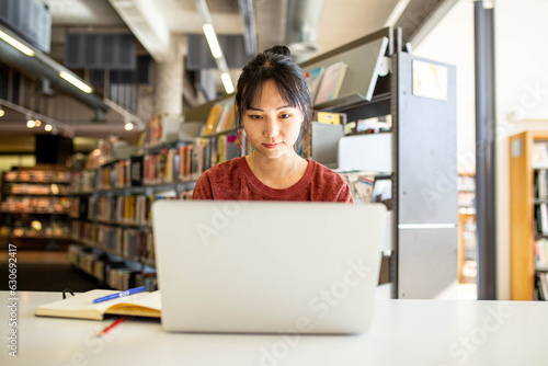 Young adult asian woman at the library studying and using her laptop